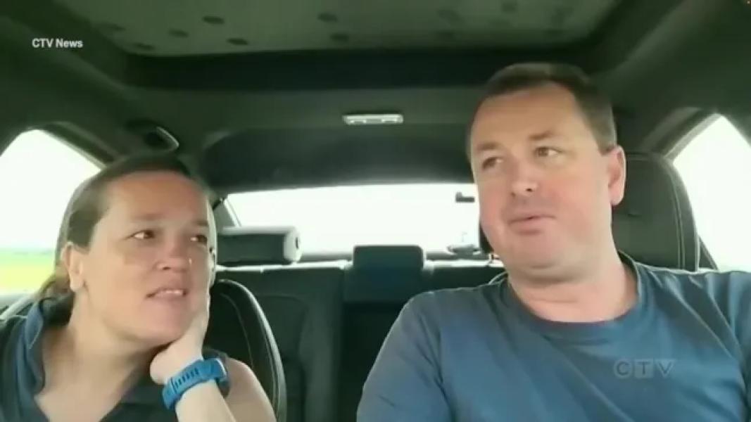 A man and a woman sit in the front seats of a car facing the viewer.