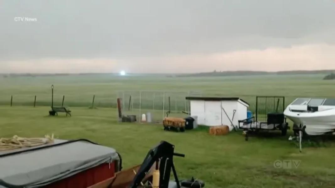 A field with vehicles in the foreground and a large ball of blue-white light hovering in the distance.