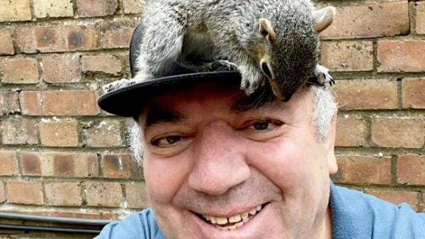 A man with a squirrel he rescued sitting on his head.